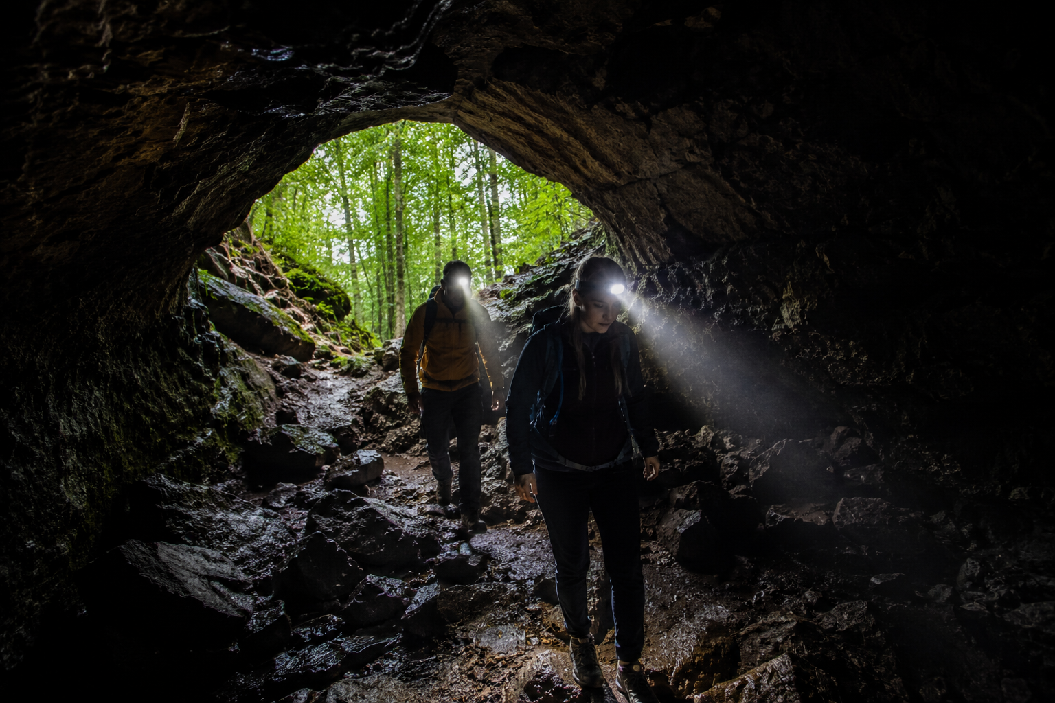 Hikers with headlamps entering a cave entrance